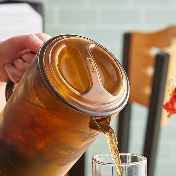 A person pouring a drink from a GET amber pitcher into a glass on a table.