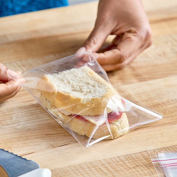 A hand holding a LK Packaging resealable plastic bag with a sandwich inside.