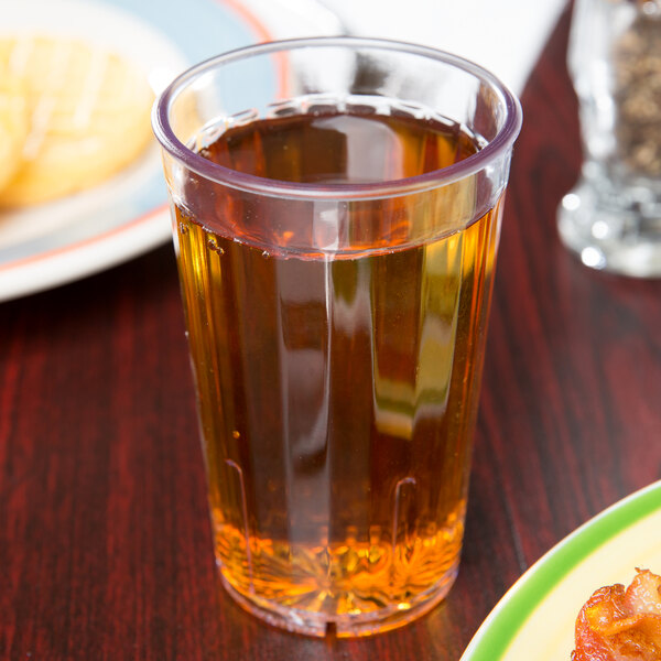 A clear GET plastic tumbler filled with a brown liquid on a table.