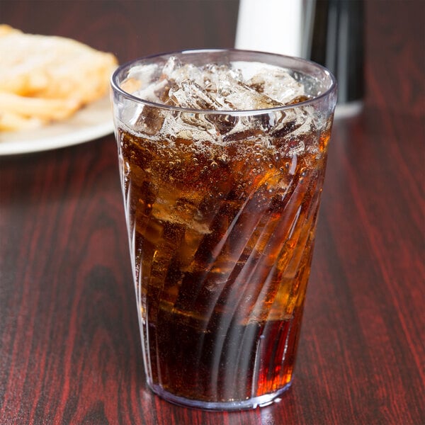 A clear plastic tumbler of ice tea with ice cubes on a table.