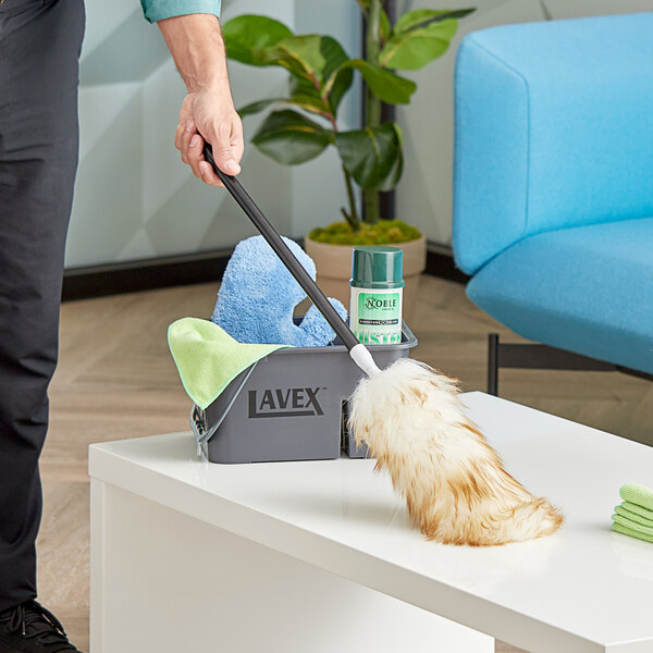 A man using a Lavex duster and a cleaning cloth to dust a table.