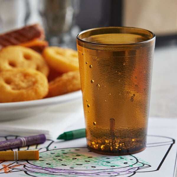 An amber plastic tumbler filled with liquid on a table with crayons.