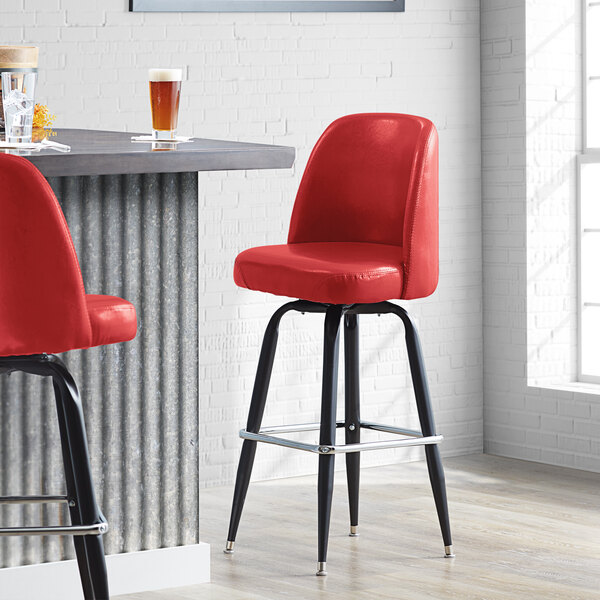 A Lancaster Table & Seating crimson vinyl bar stool with black legs.