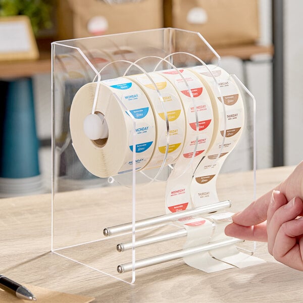A clear plastic label dispenser with three rolls of day-of-the-week stickers.