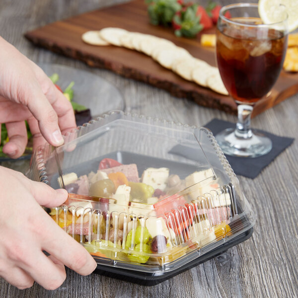 A hand holding a Genpak clear hexagonal lid on a plastic container of food.