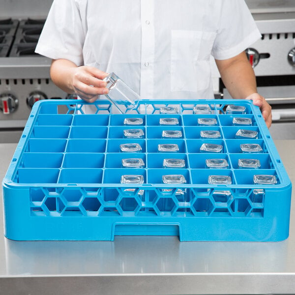 A woman in a blue apron using a Carlisle blue glass rack to hold clear glasses.