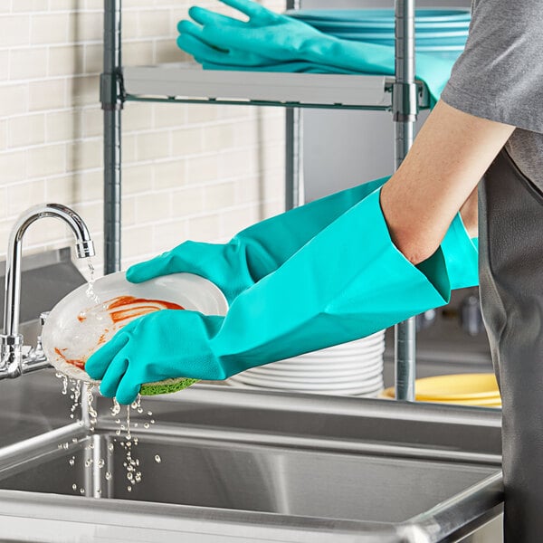 A person wearing San Jamar green nitrile gloves washing dishes in a sink.