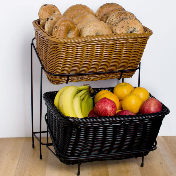 Two woven baskets on a metal stand, with the top basket holding bagels and the bottom basket containing bananas, apples, and oranges.