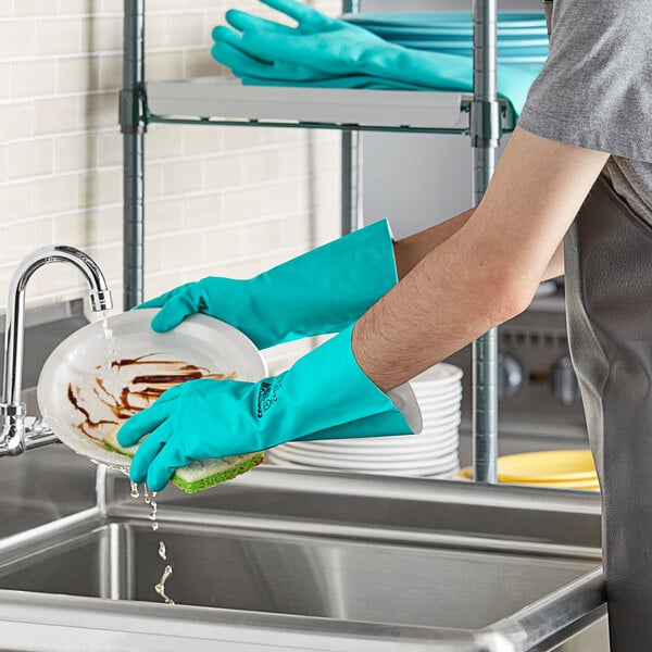A person wearing San Jamar green dishwashing gloves washing dishes on a kitchen counter.