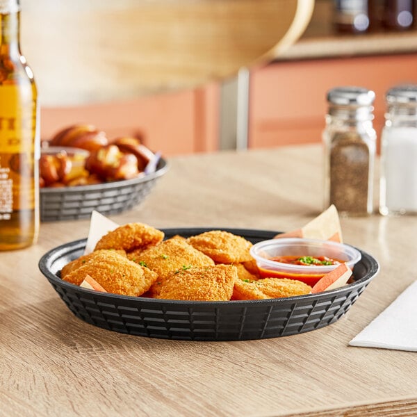 A Tablecraft black plastic diner platter and fast food basket filled with fried food on a table.