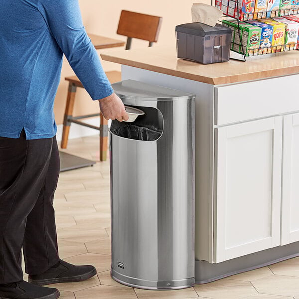 A man opening a Rubbermaid stainless steel half-round trash can in a kitchen.