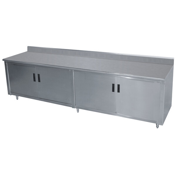 A stainless steel Advance Tabco enclosed base work table with hinged doors and a backsplash.