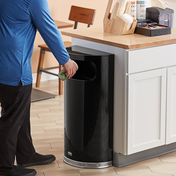 A person putting a can into a Rubbermaid half round trash can.