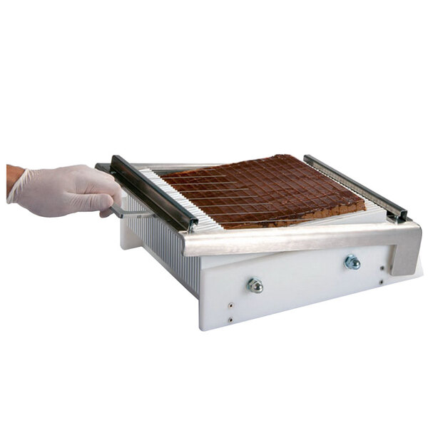 A hand using a Martellato mini guitar candy slicer to cut chocolate cake.