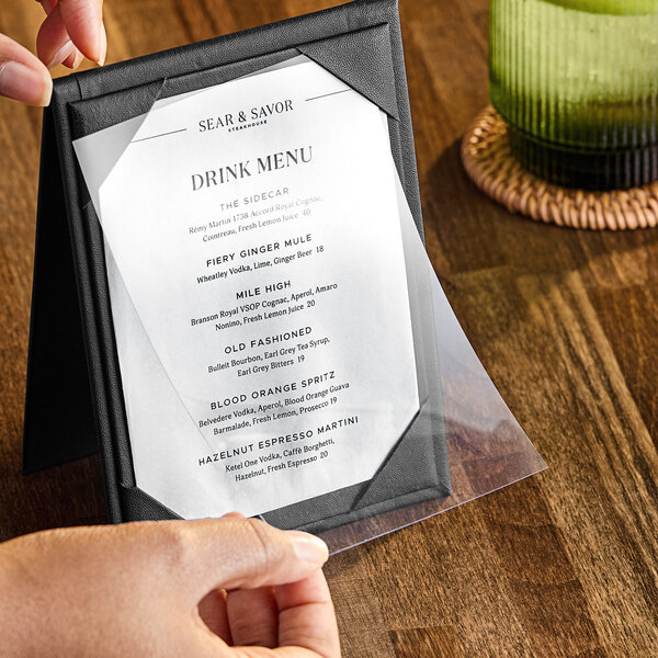 A hand holding a clear vinyl sheet protector with a menu inside.