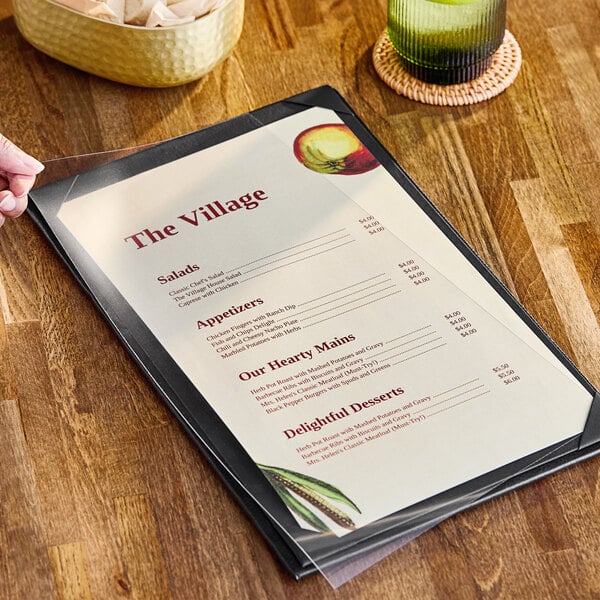 A hand holding a menu on a table with a clear vinyl sheet protector over it.