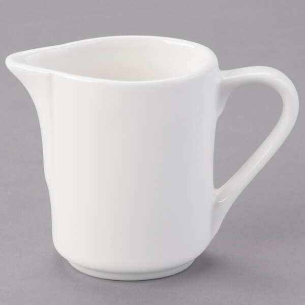 A Tuxton white china creamer pitcher with a handle.