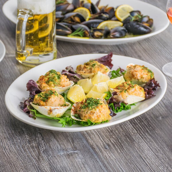 A Tuxton Modena AlumaTux Pearl White china platter with mussels and a lemon wedge on a table.