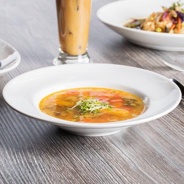 A white Tuxton soup bowl on a table with a bowl of soup and a drink.