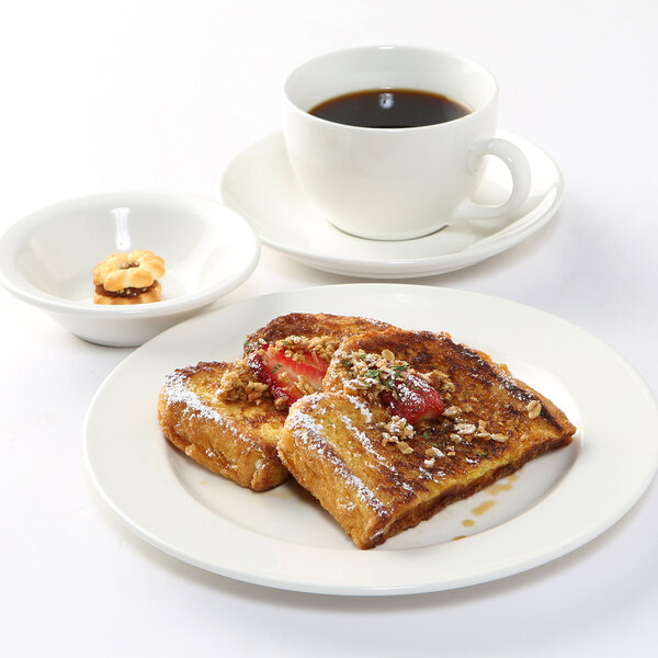 A Tuxton AlumaTux pearl white china plate with French toast and strawberries on it, next to a cup of coffee.