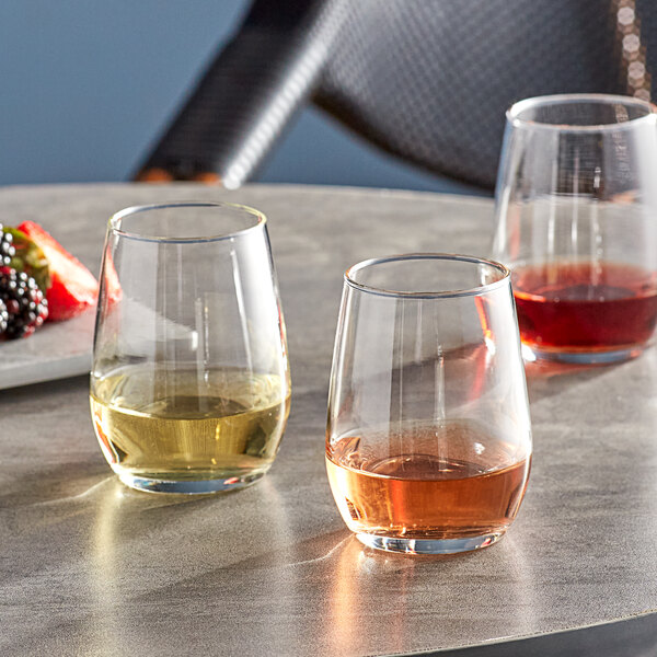 Three Libbey stemless taster glasses filled with different colored liquid on a table.