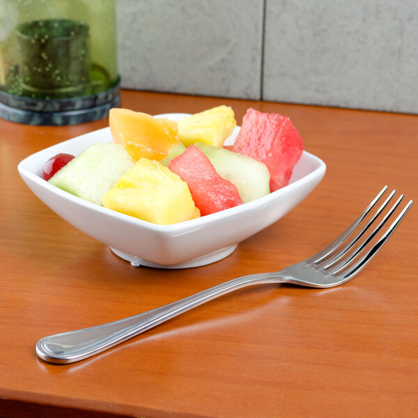 A Tuxton bright white square china bowl filled with fruit on a table with a fork.