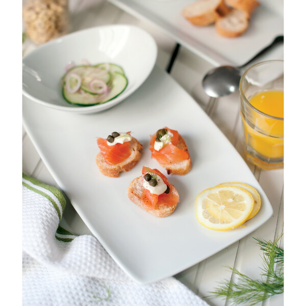 A Tuxton white rectangular china tray with food including salmon and cucumber.