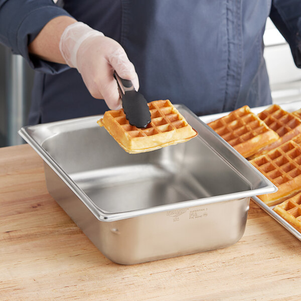 A person holding a waffle over a Vollrath stainless steel steam table pan.