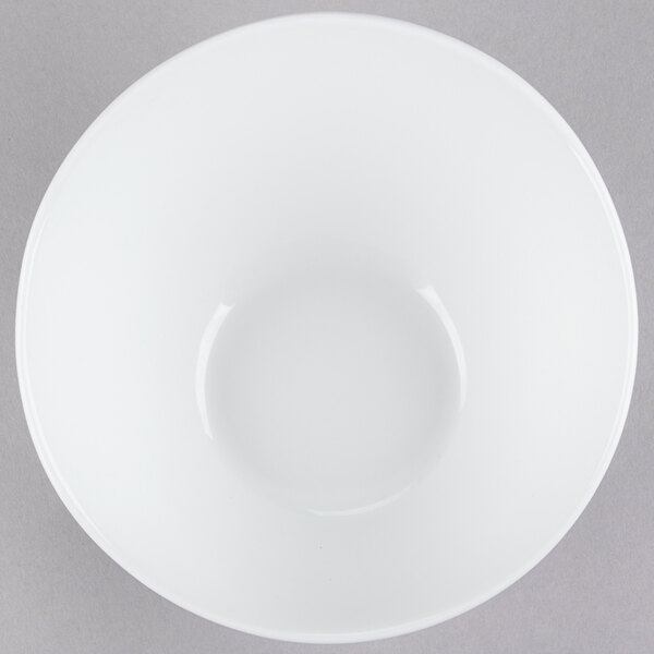 A Tuxton TuxTrendz bright white china bowl with a slanted edge on a gray surface.