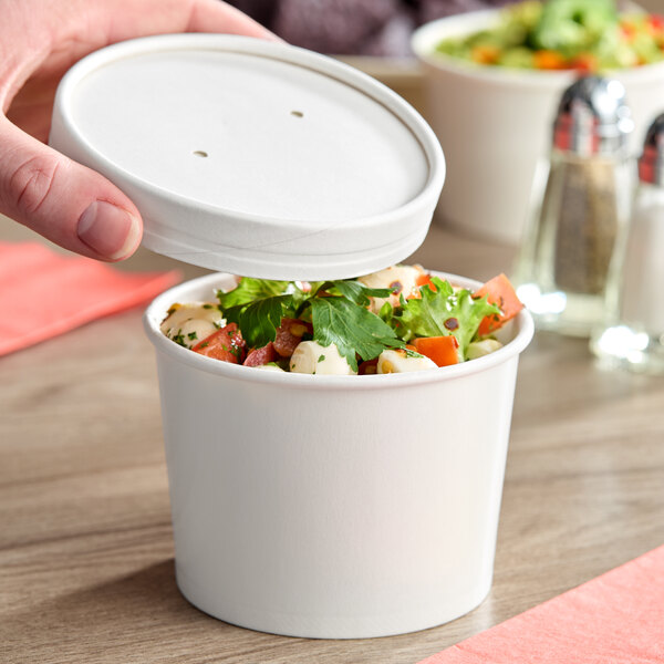 A white 12 oz. double poly-coated paper food cup with a vented paper lid, shown containing salad.