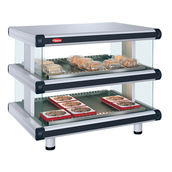 A white Hatco Granite Glo-Ray double shelf food display case on a counter with food trays inside.