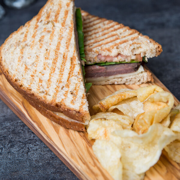 An American Metalcraft olive wood serving board with a sandwich and chips.