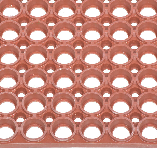 A close up of a red Notrax rubber floor mat with holes.