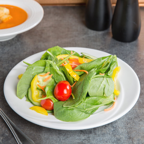 A Tuxton AlumaTux Pearl White china plate with salad, tomatoes, and peppers with a bowl of soup.