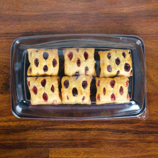 A Sabert clear plastic catering tray with a high dome lid covering pastries on a wood table.