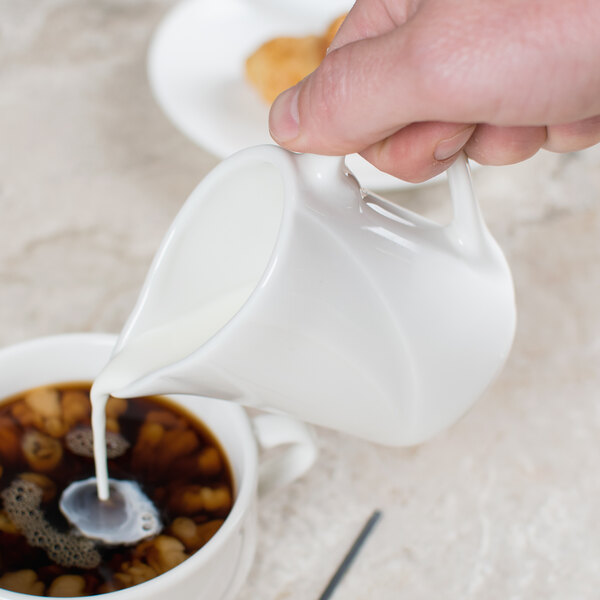 A white jug pouring milk into a cup of coffee.