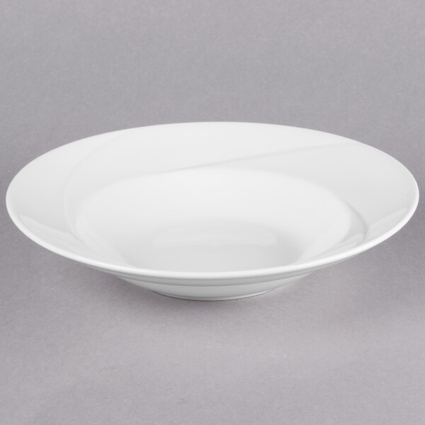 A Tuxton San Marino AlumaTux Pearl White china bowl with a curved edge on a gray surface.