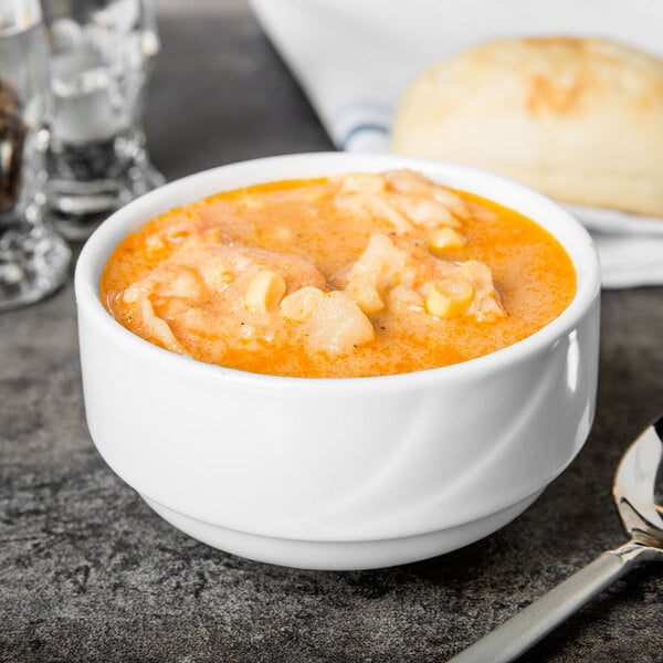 A Tuxton AlumaTux Pearl White China stackable soup cup filled with soup next to bread and a spoon.