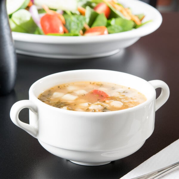 A Tuxton AlumaTux Pearl White china soup cup filled with soup with a spoon.