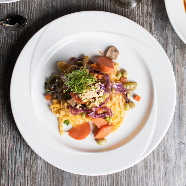 A Tuxton AlumaTux Pearl White china plate with noodles, vegetables, and sauce on it.