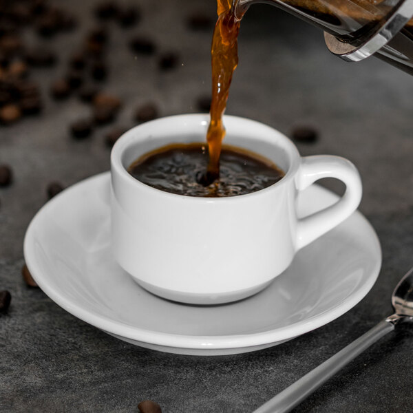 A cup of coffee being poured into a white Tuxton China saucer.