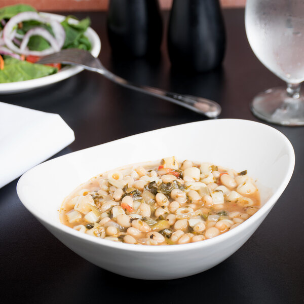 A Tuxton white china bowl filled with soup with beans and vegetables on a table.