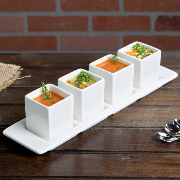 A row of soup in square white Tuxton bowls.
