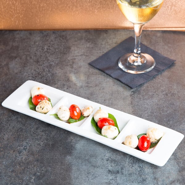 A Tuxton AlumaTux rectangular white china tray with 4 compartments on a table with a plate of food.