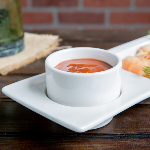 A white Tuxton AlumaTux ramekin filled with sauce on a plate of food with shrimp and vegetables.