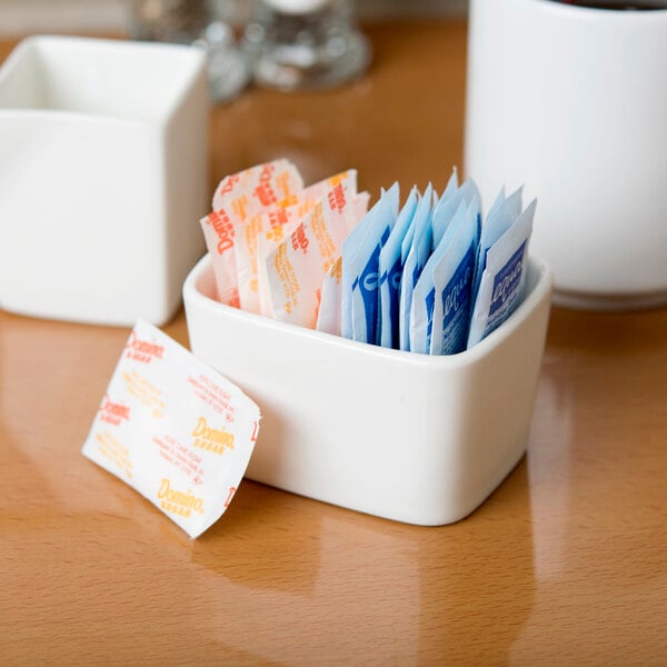 A white Tuxton china sugar packet holder on a white surface filled with sugar packets.