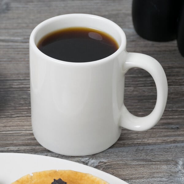 A close up of a Tuxton AlumaTux Pearl White china mug with brown liquid in it.