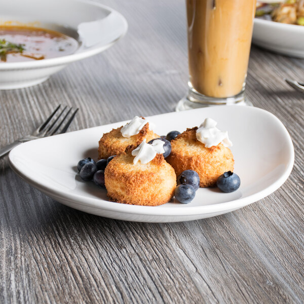 A close up of food on a Tuxton AlumaTux Pearl White ellipse plate with a drink and a bowl of soup.