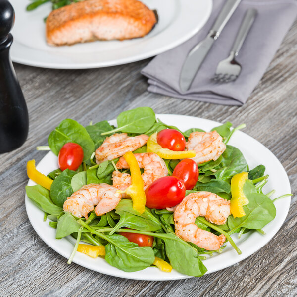 A Tuxton AlumaTux Pearl White china plate with a shrimp and spinach salad with tomatoes and peppers on a table.