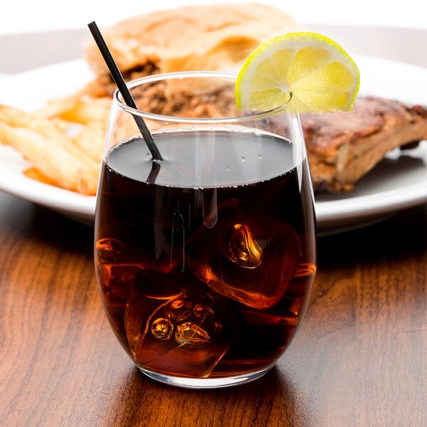 A Chef & Sommelier double old fashioned glass with brown liquid, ice, and a lemon wedge on a plate of meat.